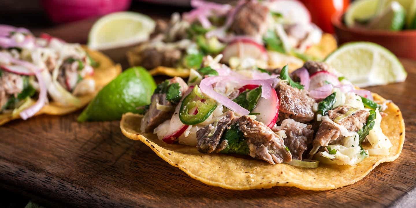 Mais-Taco auf einem Holzbrettchen mit Fleischfüllung und Radieschen, Zwiebeln und Jalapenos als Tapping.