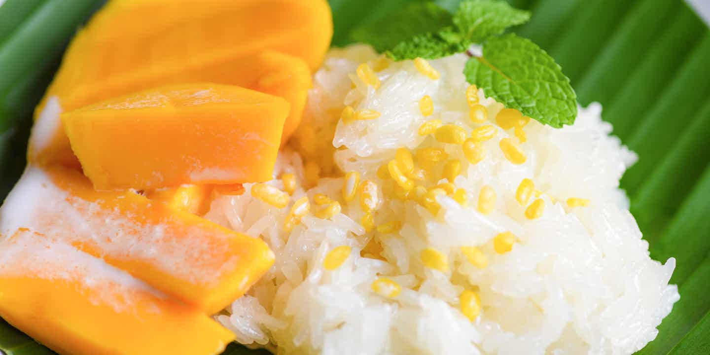 Frische leuchtend gelbe Mangostücke auf gekocktem Klebereis garniert mit gelben Körnern und einem Minz-Zweig