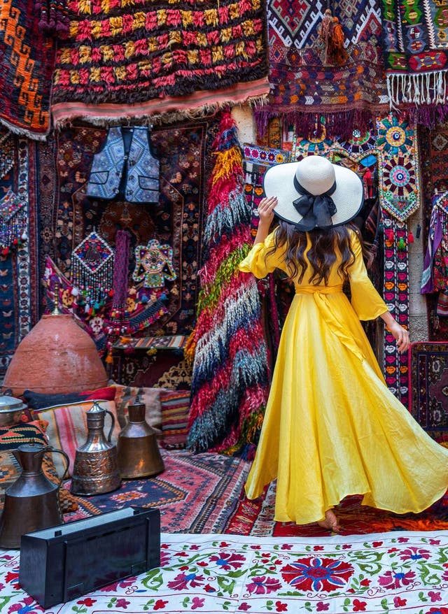 Shopping Istanbul Frau in gelbem Kleid vor zahlreichen Teppichen