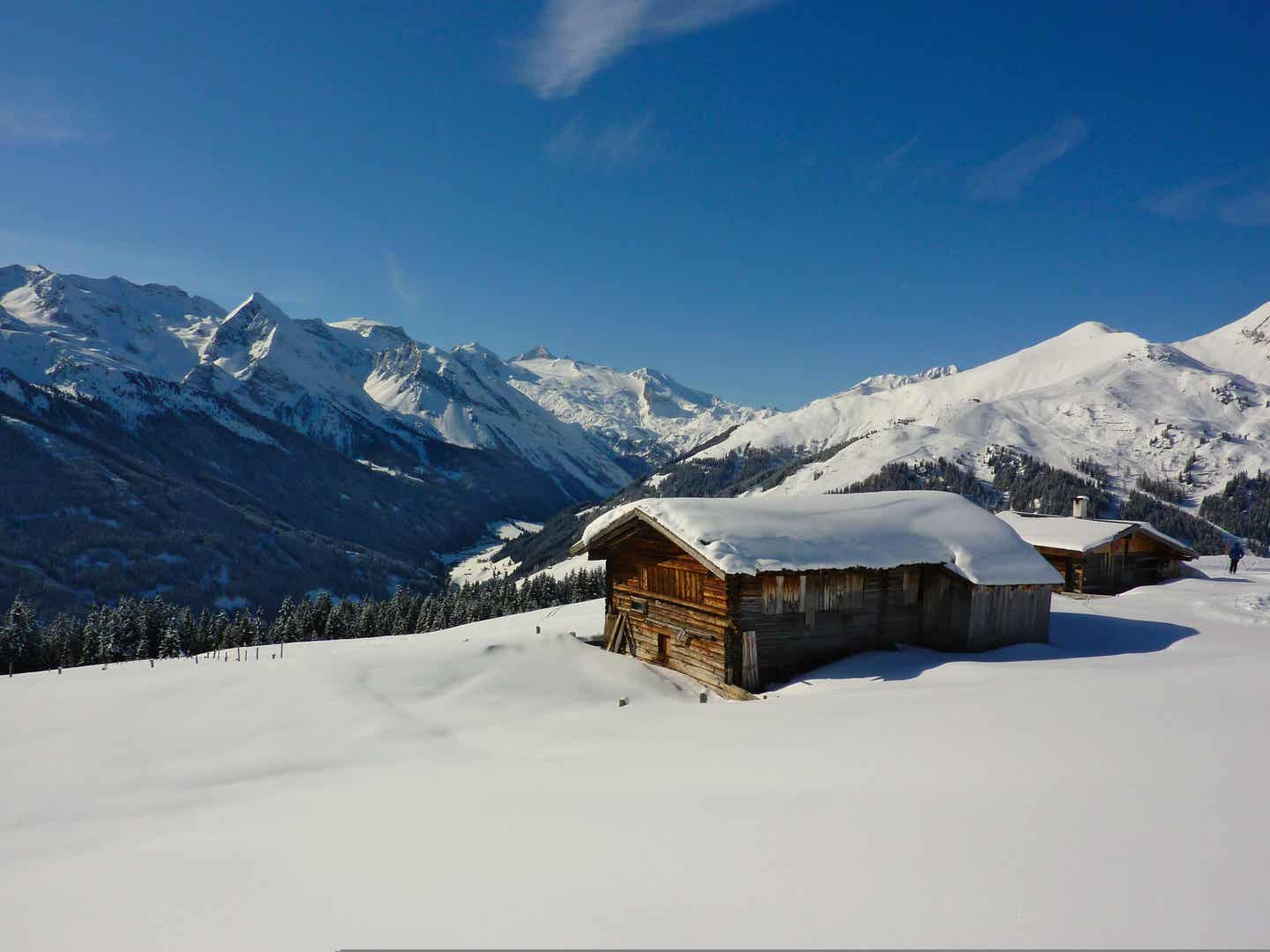 Eine schneebedeckte Hütte vor winterlicher Bergkulisse – ein typisches Bild für Skifahrer