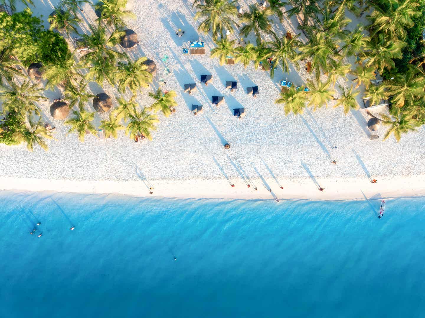 Luftaufnahme vom Sandstrand in Kendwa, Sansibar mit grünen Palmen, Sonnenschirmen und klarem Wasser des Indischen Ozeans bei Sonnenuntergang
