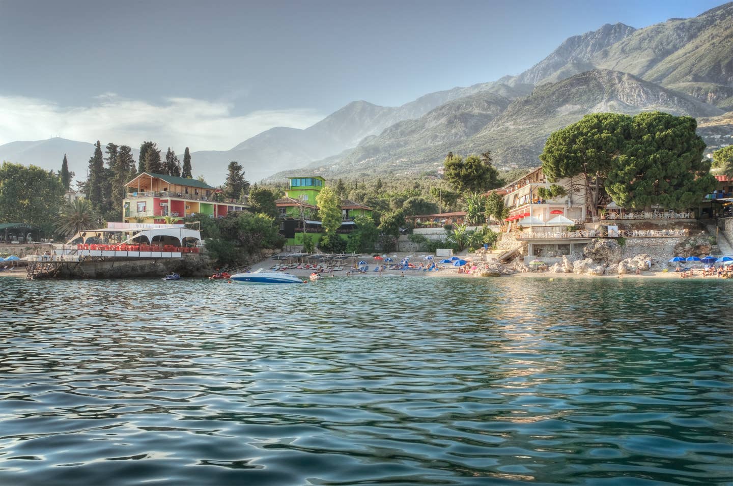 Albanien Urlaub mit DERTOUR. Strand von Dhermi mit Booten im Wasser und Bergen im Hintergrund