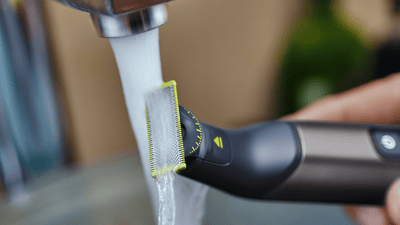 A Philips OneBlade Pro is rinsed under a running tap.