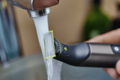 A Philips OneBlade Pro is rinsed under a running tap.