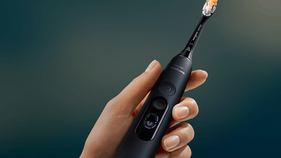 A person holds a dark blue Philips electric toothbrush in their hand.