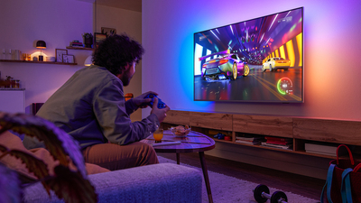 A racing video game is displayed on a Philips Ambilight TV in a dimly lit room