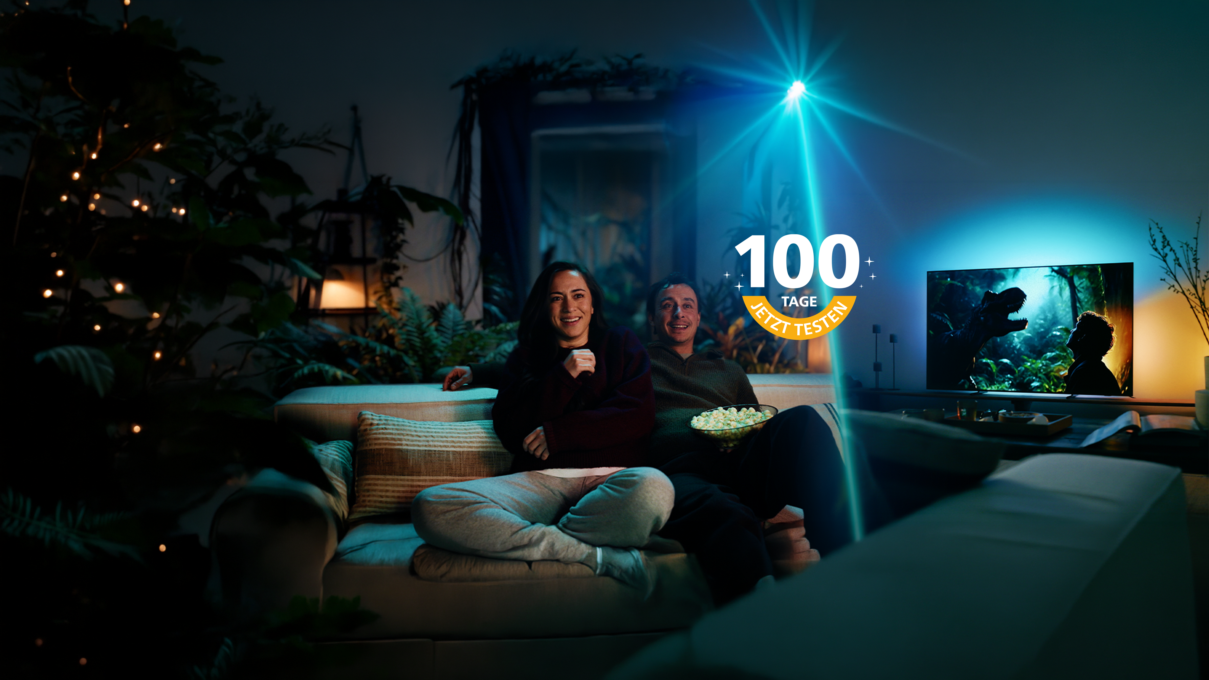 Zwei Personen sitzen auf einem Sofa und sehen auf einen Philips Ambilight TV, dessen stimmungsvolle Hintergrundbeleuchtung das Filmerlebnis in den Raum erweitert.