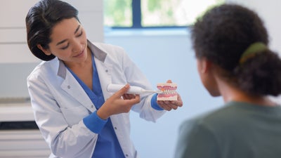 Une jeune dentiste montre à son patient comment se brosser les dents.
