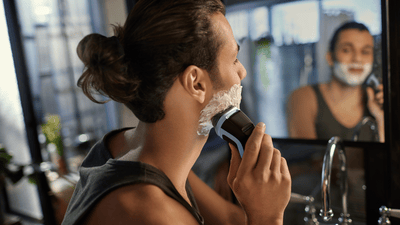 Mies, jolla on man bun-kampaus, ajelee paksua partaansa kylpyhuoneen peilin edessä.