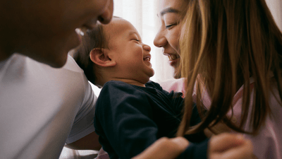 A new mom smiling at her baby with their faces close to each other. The dad is next to them.