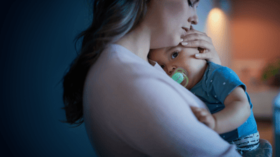 A woman gently holds her baby close to her chest. The baby, wearing a Philips Avent soother, gazes at the camera.