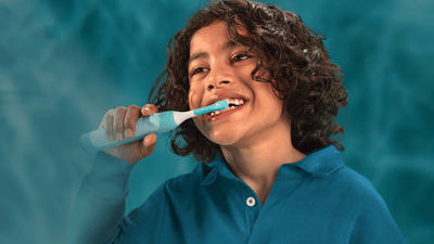 A young boy with curly hair brushes his teeth with a Philips Sonicare for Kids toothbrush.