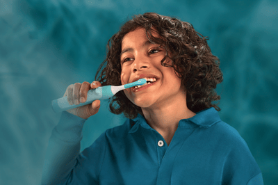 A young boy with curly hair brushes his teeth with a Philips Sonicare for Kids toothbrush.