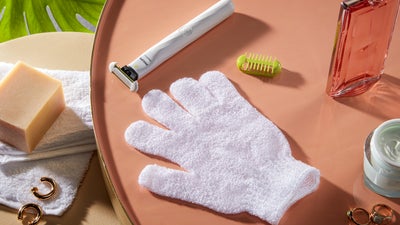 De Philips OneBlade Intimate ligt naast een witte scrubhandschoen, de opzetkam en een stuk zeep.
