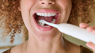A young woman with curly hair is brushing her teeth and tongue with a Philips electric toothbrush.