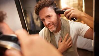 A man looks in the mirror while using his Philips Hairclippers on his hair.