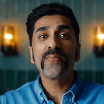 A man with a horseshoe style mustache is starting directly at the camera.