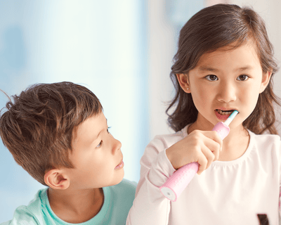 Two kids brushing with Sonicare For Kids at a sink.