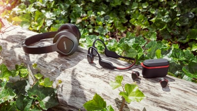 Philips sportowe słuchawki nauszne i douszne zaprezentowane na zewnątrz, umieszczone na pniu drzewa wśród zieleni.