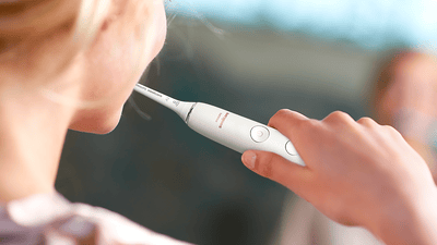A blonde woman is shown from behind brushing her teeth with a white Philips electric toothbrush.