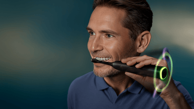 A man smiles as he brushes his white teeth using a Philips Next-Generation DiamondClean electric toothbrush.