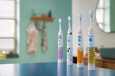 Vier elektrische tandenborstels met dierenprint voor kinderen staan op een rij op een blauw oppervlak in een badkamer.