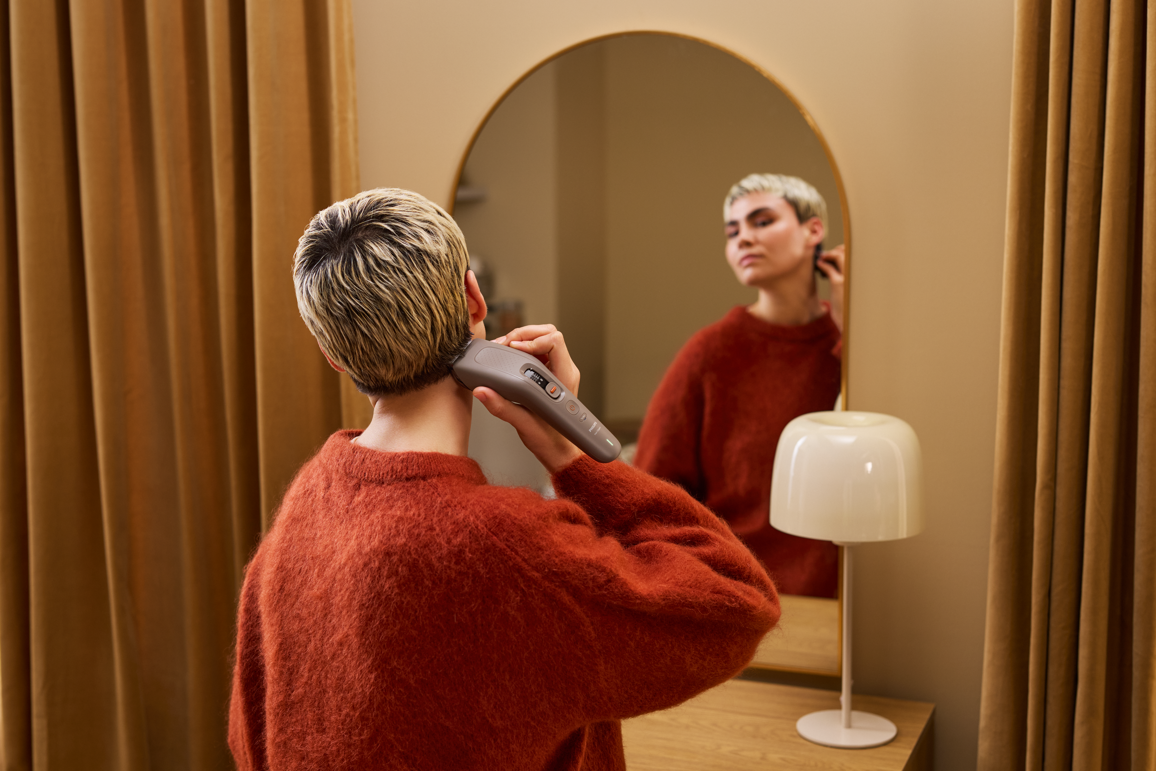 Eine Person schneidet sich mit dem Philips Haarschneider 9000 vor einem Spiegel die Haare am Hinterk...