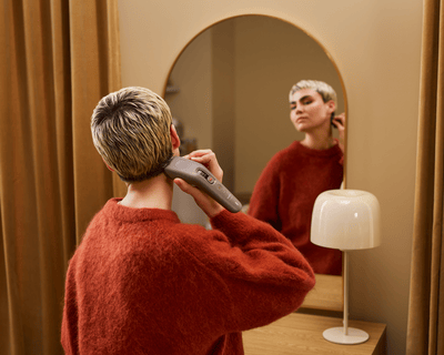 Eine Person schneidet sich mit dem Philips Haarschneider 9000 vor einem Spiegel die Haare am Hinterk...
