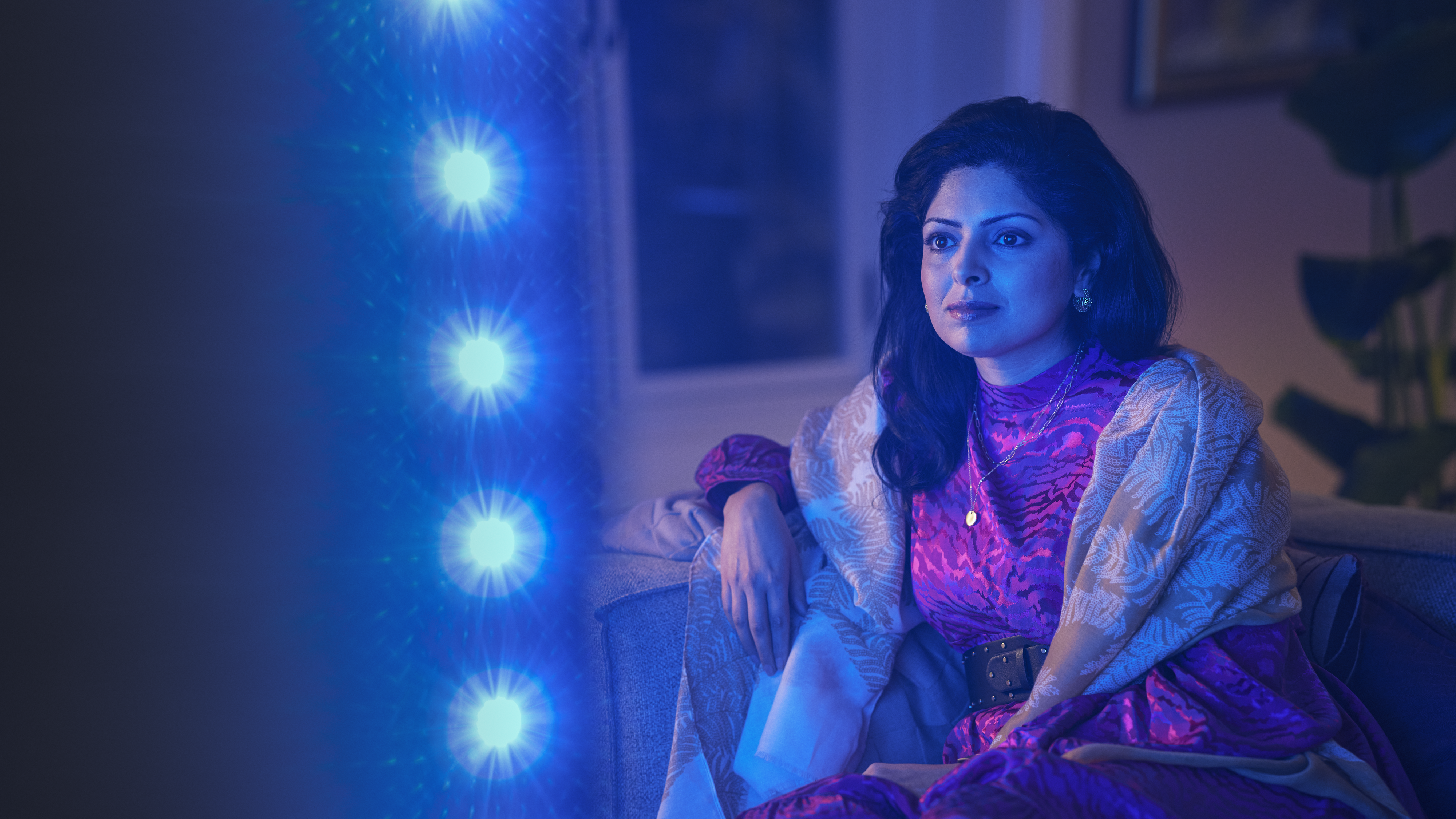 Γυναίκα που παρακολουθεί τηλεόραση Philips Ambilight, με μπλε ατμοσφαιρικό φωτισμό να αντανακλάται δίπλα στην οθόνη.