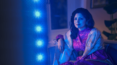 Γυναίκα που παρακολουθεί τηλεόραση Philips Ambilight, με μπλε ατμοσφαιρικό φωτισμό να αντανακλάται δίπλα στην οθόνη.