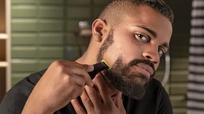 A young man looks at the camera while shaving his beard with a Philips OneBlade.