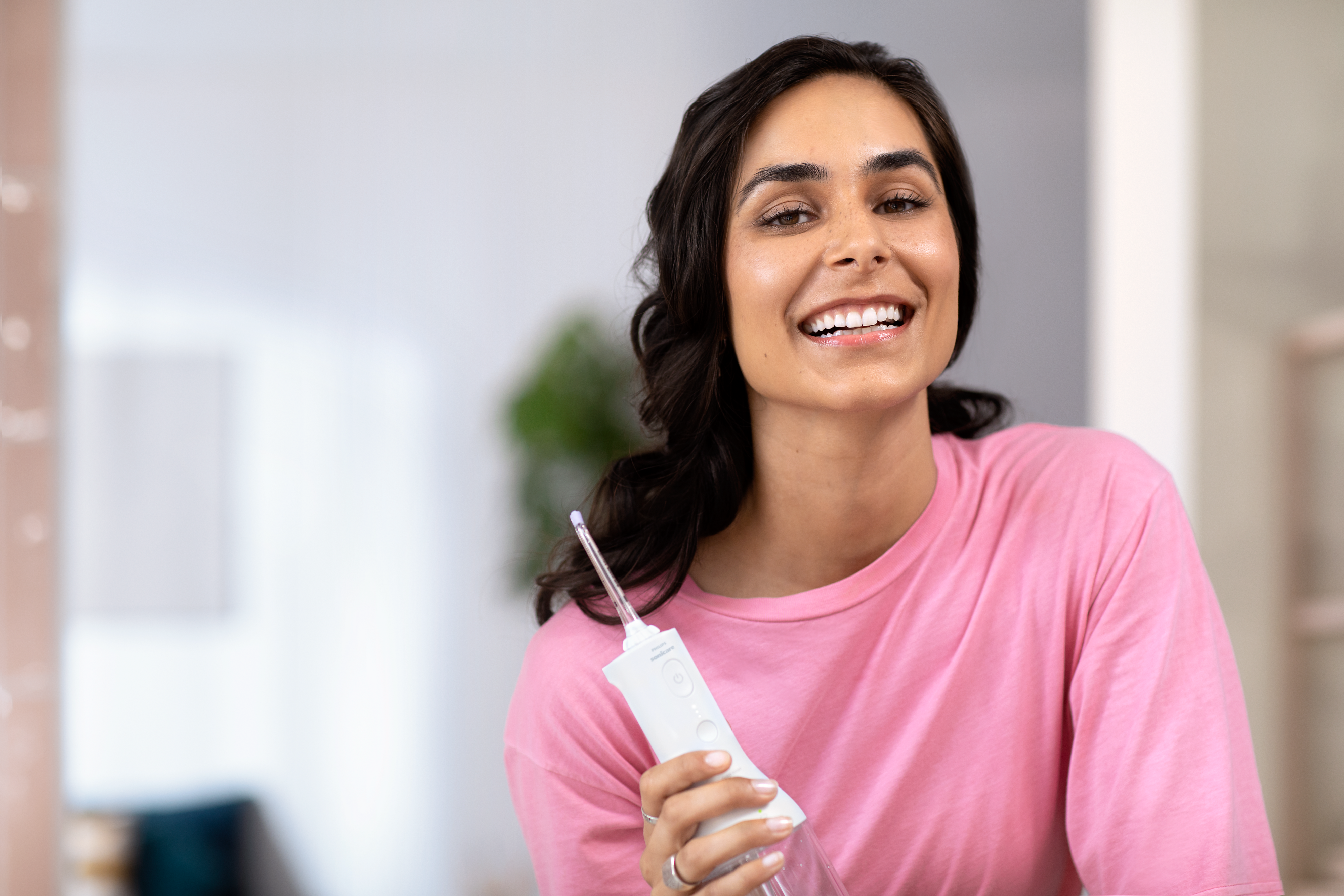 Žena držící bezdrátový zubní irigátor a usmívající se