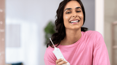 Žena držící bezdrátový zubní irigátor a usmívající se