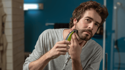 A man looks at the camera while shaving his beard with a Philips OneBlade.