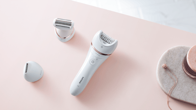 A product image of a Philips epilator and attachments on a light pink table.