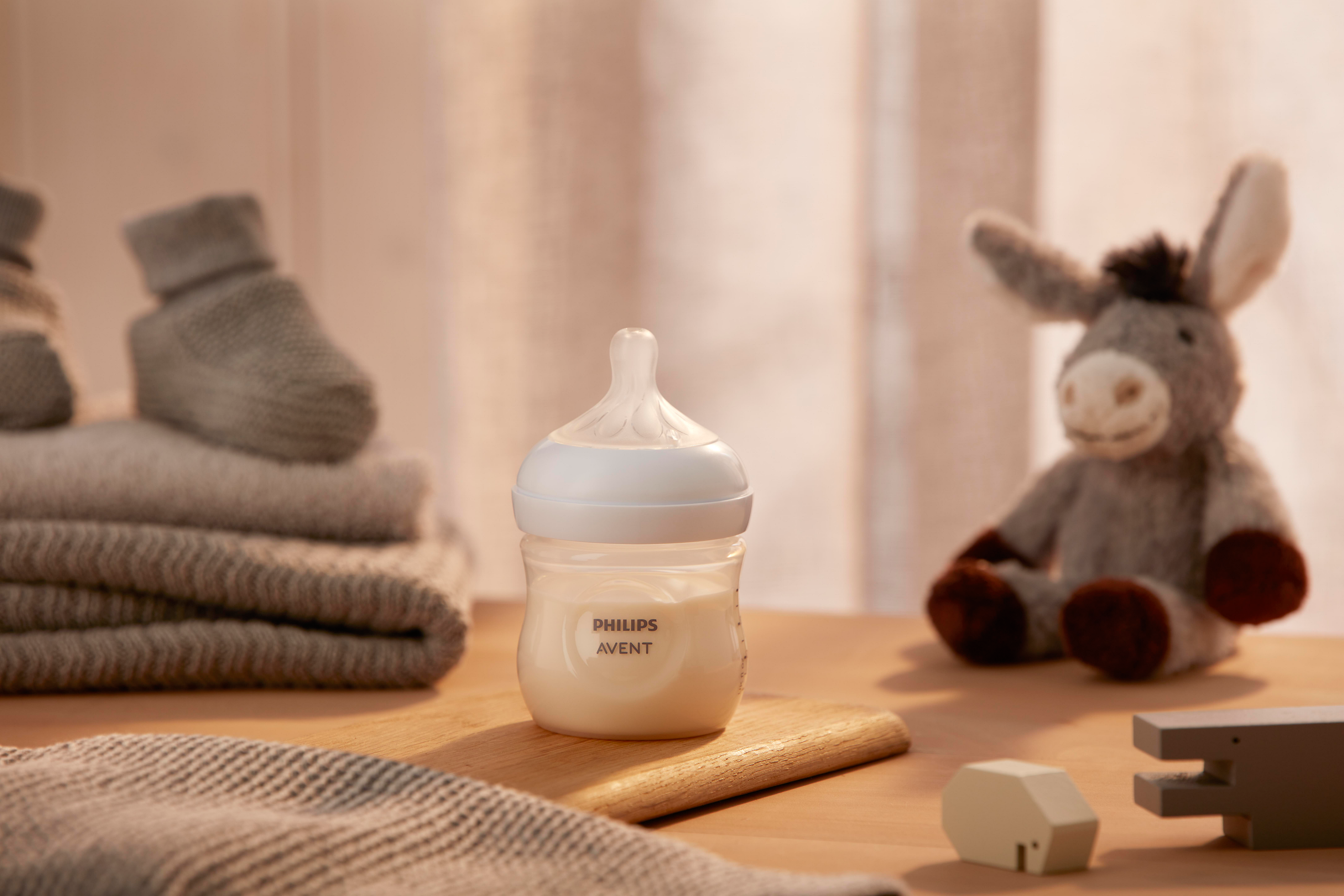 Product image of a Philips Avent Natural Response baby bottle in front of a toy donkey on a wooden surface.