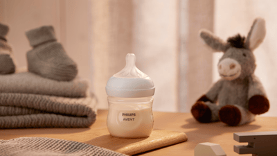 Product image of a Philips Avent Natural Response baby bottle in front of a toy donkey on a wooden surface.