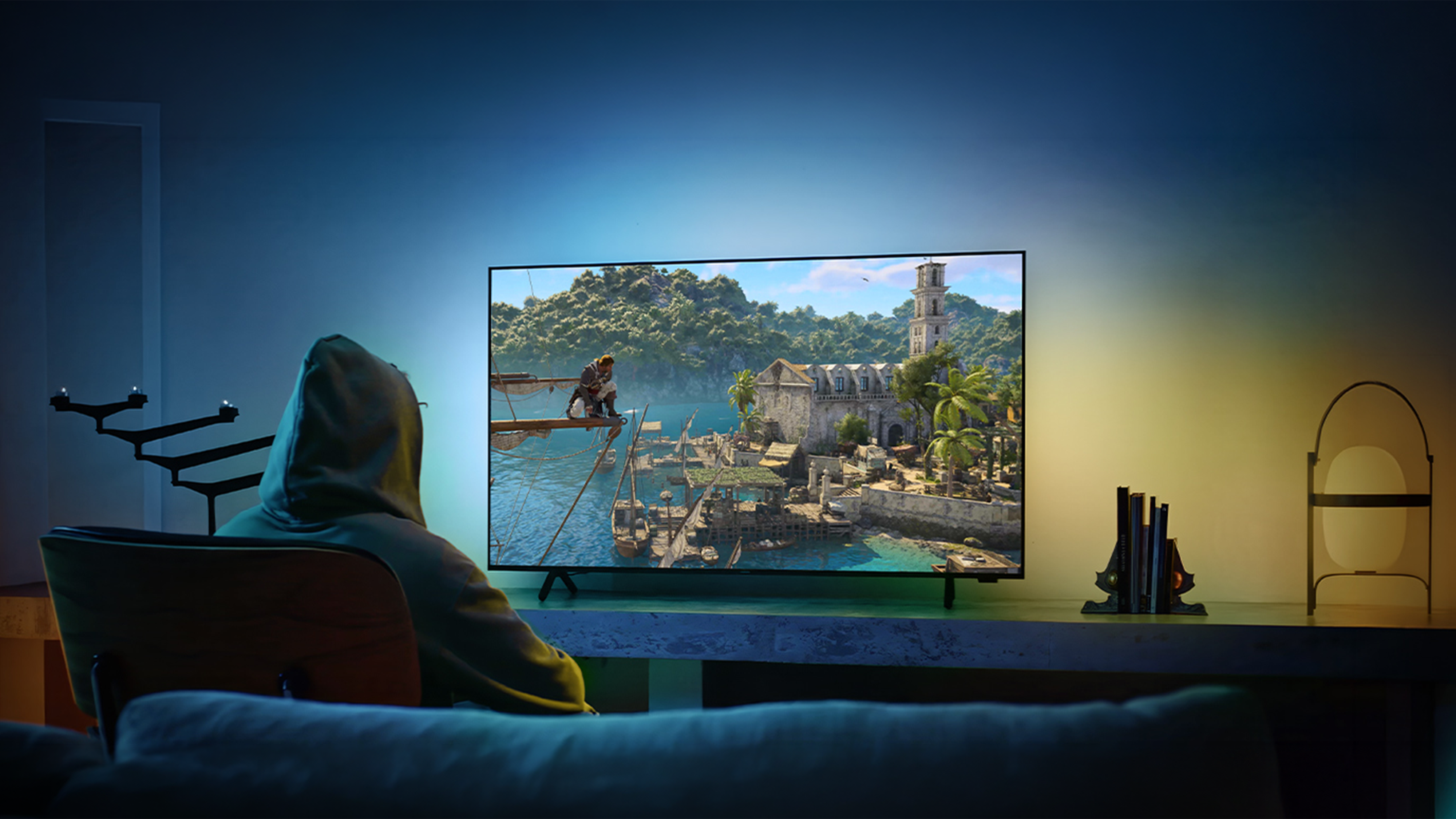 Person spielt Assassin’s Creed auf einem Philips Ambilight TV in einem stimmungsvoll beleuchteten Wohnzimmer.