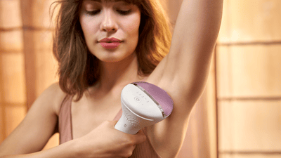 A young woman with shoulder long brown hair is using her pink Philips IPL Lumea on her underarms.