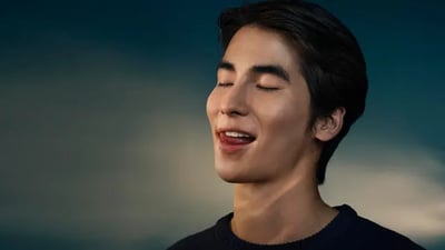 A young man smiles as he licks his white teeth against a dark gradient background.