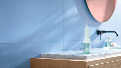A Philips water flosser is shown stood on a bathroom counter in a blue bathroom.