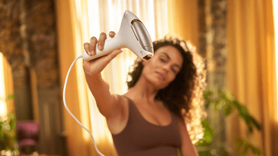 A young woman with dark curly hair is holding a Philips Lumea IPL device into the camera.
