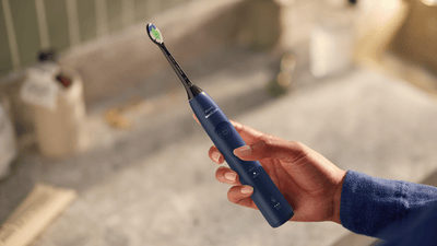A person holds a dark blue Philips electric toothbrush in their hand.