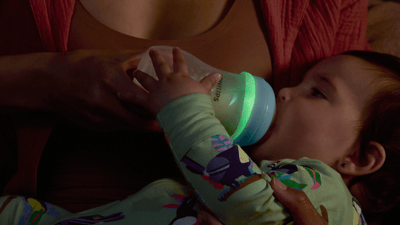 A close-up shot of a woman feeding her newborn using a Philips Natural Response Nighttime bottle.