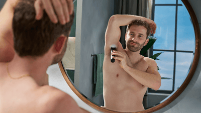 Ein Mann rasiert sich vor dem Badezimmerspiegel mit dem Philips Bodygroom die Achseln.
