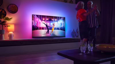 Par pleše u dnevnoj sobi dok gleda Philips Ambilight TV s raznobojnim ambijentalnim osvjetljenjem.