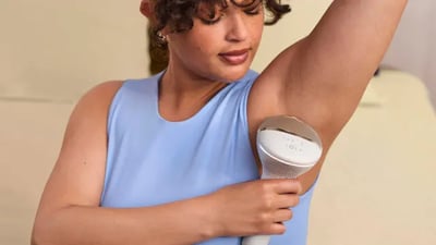 A close-up of a curly haired woman using a Philips Lumea IPL device on her underarms.