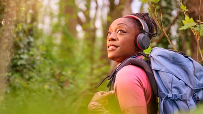 Donna che cammina in una foresta con uno zaino blu, indossa le cuffie Philips A6219 e alza lo sguardo con un sorriso