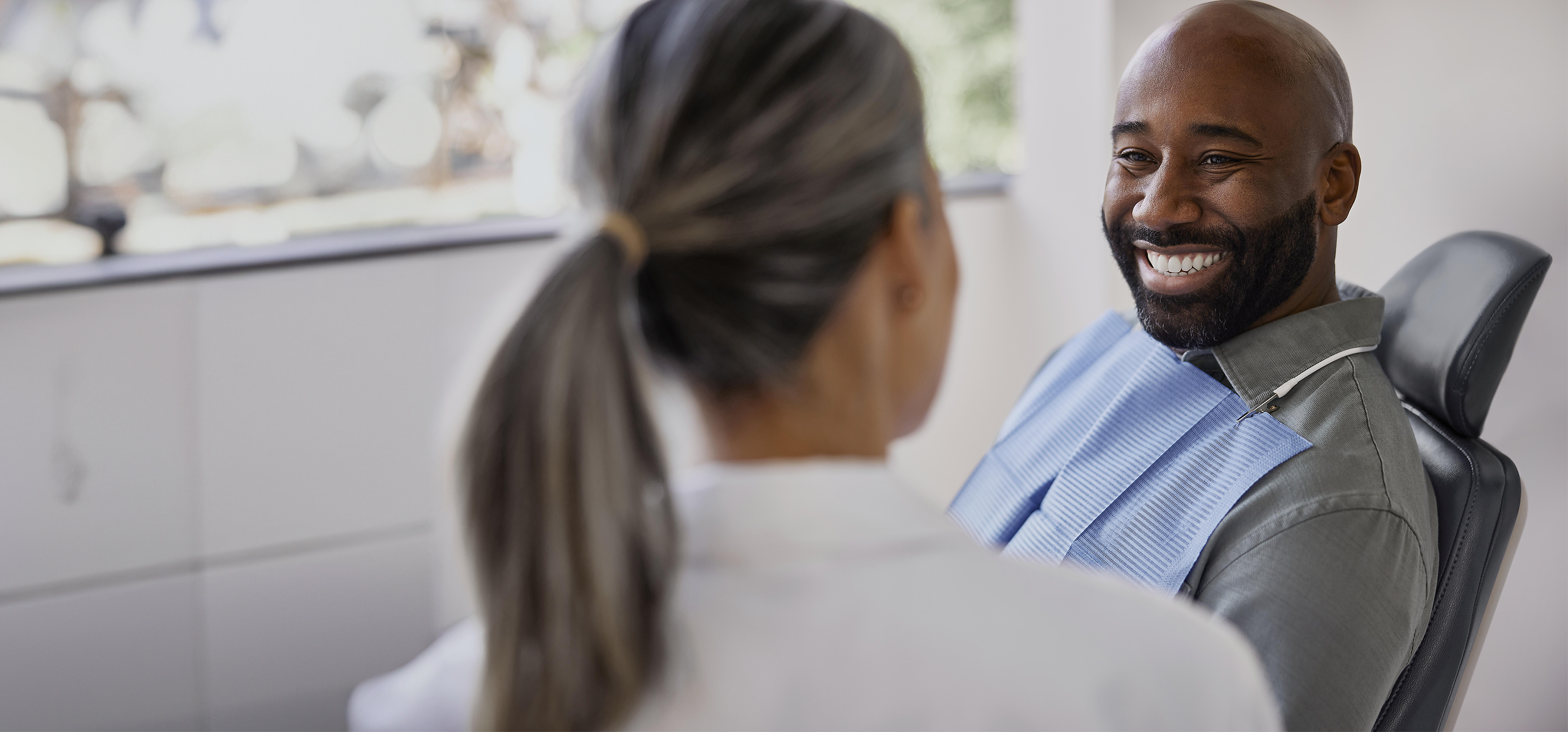 A paitent in a dental chair smiling at a dental professional.