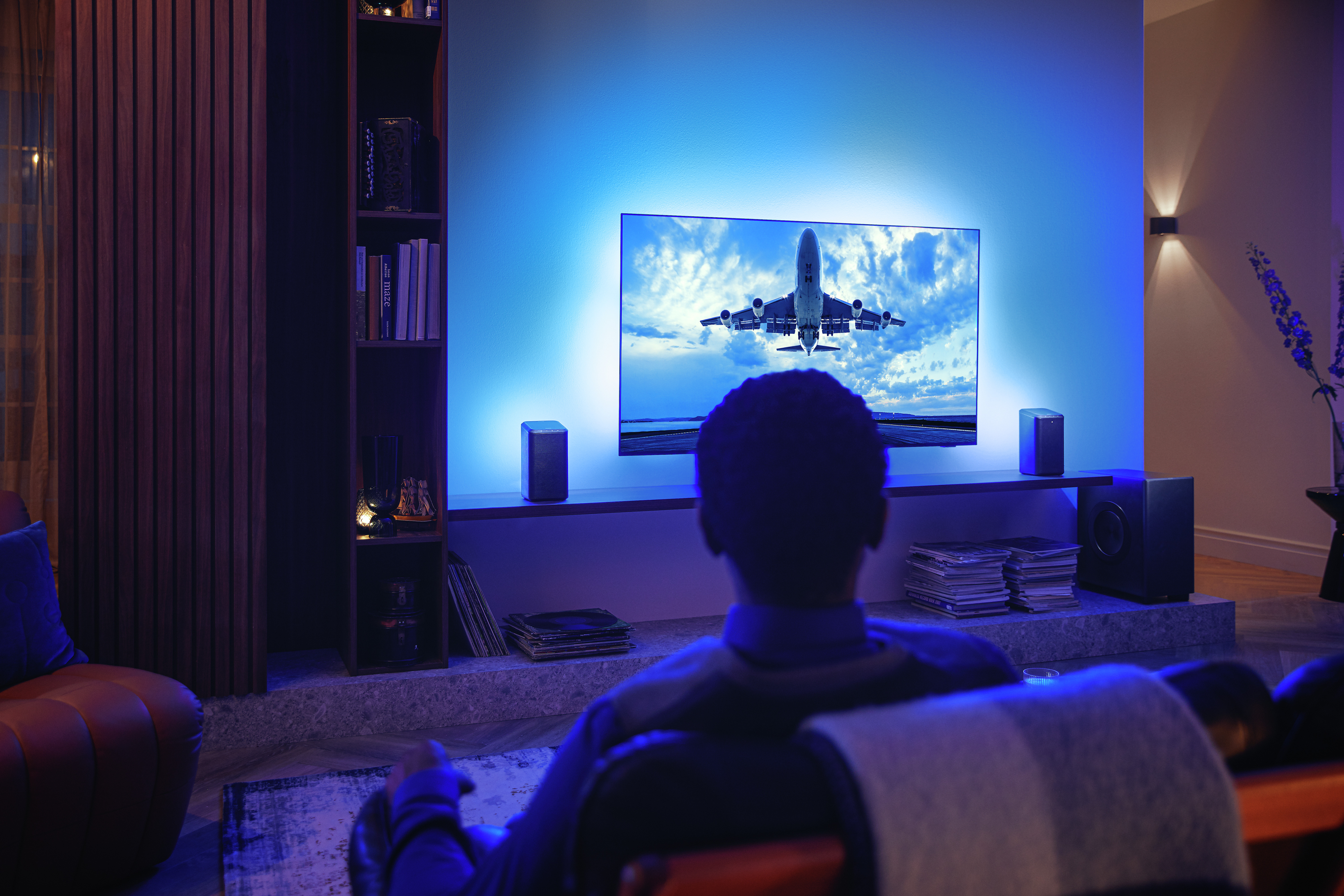 Muškarac uživa u svom Philips Ambilight TV-u povezanom s Wi-Fi zvučnicima
